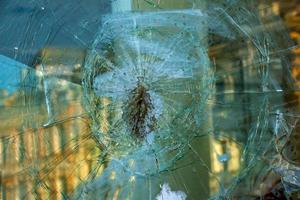 A hole in the window glass with a bullet during a military shooting. Cracks propagate around the hole. Dirty window frame. View of the street from the inside. photo