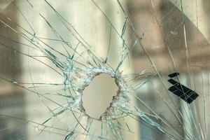 A hole in the window glass with a bullet during a military shooting. Cracks propagate around the hole. Dirty window frame. View of the street from the inside. photo