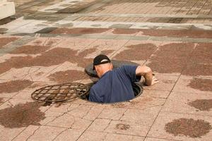 A worker climbs out of an open manhole in the road. Dangerous open unprotected manhole on the road. Accident with a sewer manhole in the city. The concept of repairing underground utilities. photo