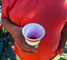 un Envejecido hombre sostiene un vaso de recién exprimido granada jugo en su mano. foto