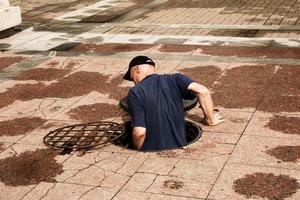 A worker climbs out of an open manhole in the road. Dangerous open unprotected manhole on the road. Accident with a sewer manhole in the city. The concept of repairing underground utilities. photo