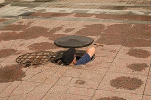 A worker climbs out of an open manhole in the road. Dangerous open unprotected manhole on the road. Accident with a sewer manhole in the city. The concept of repairing underground utilities. photo