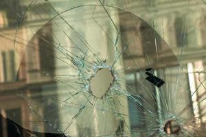 un agujero en el ventana vaso con un bala durante un militar tiroteo. grietas propagar alrededor el agujero. sucio ventana marco. ver de el calle desde el adentro. foto