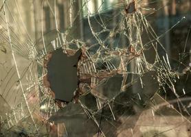 A hole in the window glass with a bullet during a military shooting. Cracks propagate around the hole. Dirty window frame. View of the street from the inside. photo