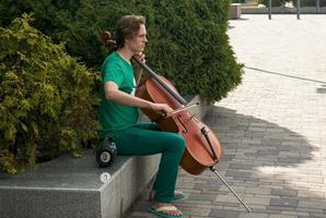 un joven hombre obras de teatro el violonchelo en el ciudad parque. foto