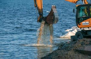 Dnepropetrovsk, Ukraine - 11.26.2021 Excavator works to strengthen the embankment. Hydraulic excavator working on the river bank. photo