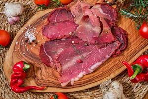 Cured meat, bacon or Turkish pastirma on cutting board with vegetables and spices, meat dish traditional Turkish food for sunday breakfast photo