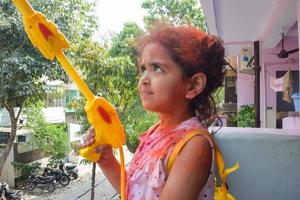 Sweet little Indian girl playing colours on Holi festival, holding pichakaree full of colours, Holi festival celebrations in Delhi, India photo