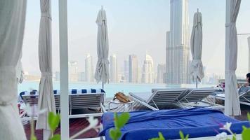 Dubai, UAE, 2022- tourist lay relax enjoy luxury vacation by rooftop pool with skyline background. Luxury holiday destination famous Sky view tower hotel video