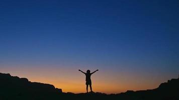 Happy celebrating winning success woman at sunset or sunrise standing elated with arms raised up in celebration of having reached mountain top summit goal during hiking travel trek