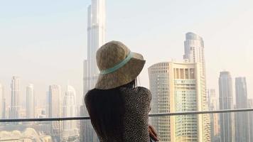 Dubai, UAE, 2022 - Modern tourist female traveler looking at Burj Khalifa tower against hazy white sky, Dubai, UAE video