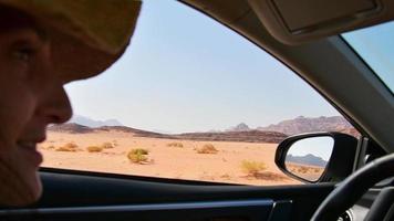 Front seat view caucasian woman tourist excited drive rented car with Wadi Rum desert background from window. Road trip in Jordan, middle east explore. Car insurance and holidays abroad while on trip video