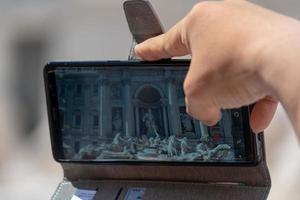 Selfie con smartphone en la fontana de Trevi llena de turistas Roma Italia foto