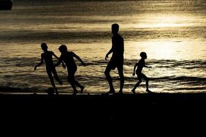 silueta de negro para niños jugando fútbol a el playa a puesta de sol foto