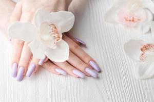 manos de niña con delicada manicura púrpura y flores de orquídeas foto