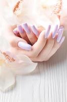 manos de niña con delicada manicura púrpura y flores de orquídeas foto