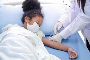 A doctor injects a vaccine in the arm of an African-American girl lying in a hospital bed. To strengthen immunity and protect it from various illnesses. Concept of the vaccine against COVID-19 photo