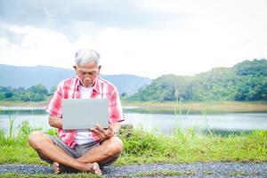 mayor hombres asiáticos sentar y tipo en cuadernos a trabajo al aire libre en el natural parque. el concepto de un Jubilación comunidad foto