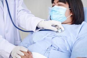 Doctors used a stethoscope to examine the health of a fat woman, wearing a mask, lying on a hospital bed. Treatment of patients during the coronavirus epidemic. Concept of medical service photo