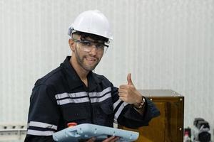 retrato de un indio masculino ingeniero con casco y la seguridad lentes demostración pulgares arriba foto