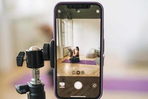joven mujer con pequeño hija aptitud blogger haciendo ejercicios y grabación vídeo en móvil teléfono en estudio foto