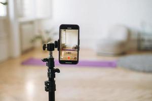 Mobile phone on tripod in empty living room with fitness mats on the floor photo