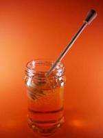 Honey jar with spindle spoon on orange background photo