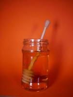 Honey jar with spindle spoon on orange background photo