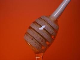 Liquid honey on a spindle spoon on an orange background photo