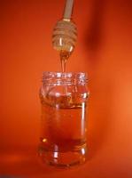 Honey jar with spindle spoon on orange background photo