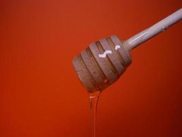 líquido miel en un huso cuchara en un naranja antecedentes foto