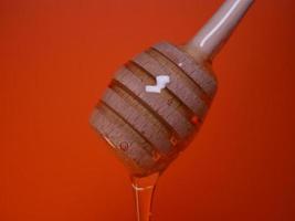 Liquid honey on a spindle spoon on an orange background photo