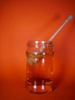 Honey jar with spindle spoon on orange background photo