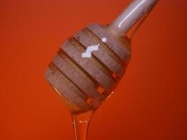 líquido miel en un huso cuchara en un naranja antecedentes foto