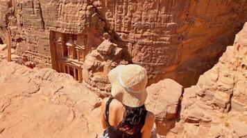 Close up Caucasian tourist traveler sit on viewpoint above Petra ancient city looking at the Treasury or Al-khazneh, famous travel destination of Jordan. UNESCO World Heritage site video