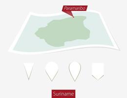 curvo papel mapa de Surinam con capital paramaribo en gris antecedentes. cuatro diferente mapa alfiler colocar. vector