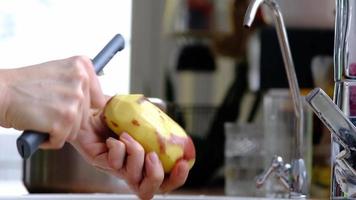 kvinnors händer skala rå potatisar med en särskild kniv med en vegetabiliska skalare under en ström av vatten i de kök. matlagning, sparande vatten, miljövänlig använda sig av av Resurser video