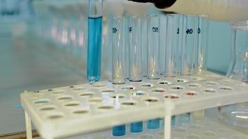 estudiar de un azul sustancia en un prueba tubo. un científico en un laboratorio pone un corcho en un trípode con un azul sustancia para investigación. video