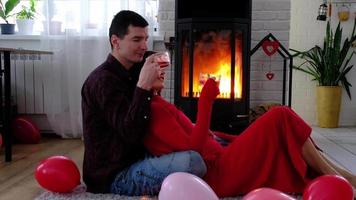 homme et femme amoureux à la maison sont assis près du poêle à bois avec un feu brûlant sur un tapis confortable. saint valentin, couple heureux, histoire d'amour, relations video