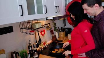 Man and woman in love date at home in kitchen they bake pancakes and happy hugs. Valentine's Day, happy couple, love story. Love nest, housing for young family video