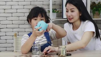mother is teaching her daughter to drop the piggy bank. savings concept video