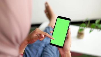 donne rilassare nel il vivente camera mentre scorrimento verde schermo smartphone video