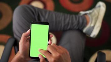 hands holding a green screen smartphone from above angle with background of men sitting on the living room video