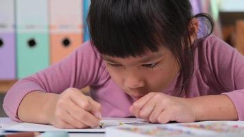 Happy little girl drawing with crayon on paper sitting at table in her room at home. Creativity and development of fine motor skills.