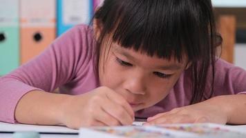 content peu fille dessin avec crayon sur papier séance à table dans sa pièce à maison. la créativité et développement de bien moteur compétences. video