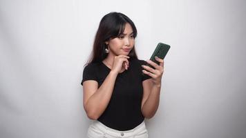A thoughtful young woman in black shirt and holding her chin with phone on hand isolated by white background video