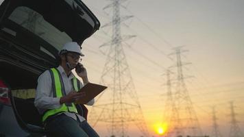 Male electrical engineer Sitting in the back of the car Use talkie radios and tablets to work on projects, working on high voltage towers in the evening or morning. video