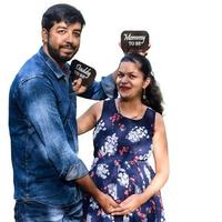 Indian couple posing for maternity baby shoot with white plain background. The couple is posing in a lawn with green grass and the woman is falunting her baby bump in Lodhi Garden in New Delhi, India photo