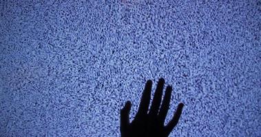 Hand crawling up a tv screen displaying no signal video