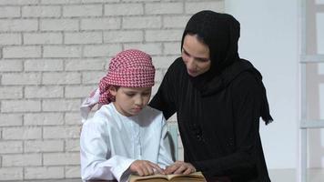 feliz madre árabe e hijo juntos sentados en el sofá y leyendo un libro. video